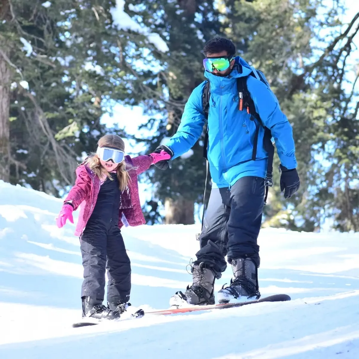 An instructor holding hands with a young student learning to snowboard in Gulmarg