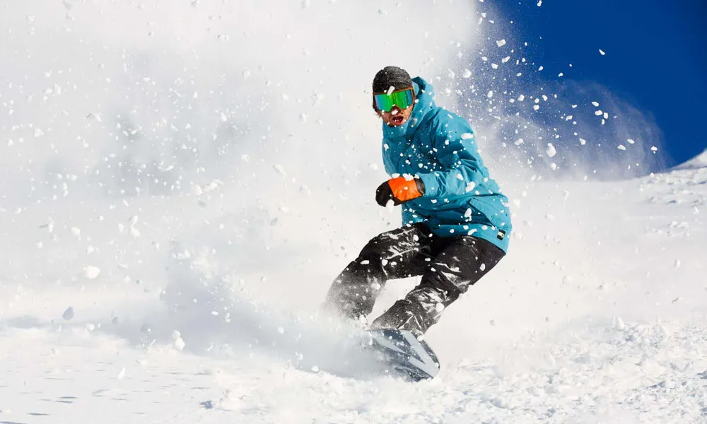 Snowboarder carving on Gulmarg alpine terrain — gear included with every course