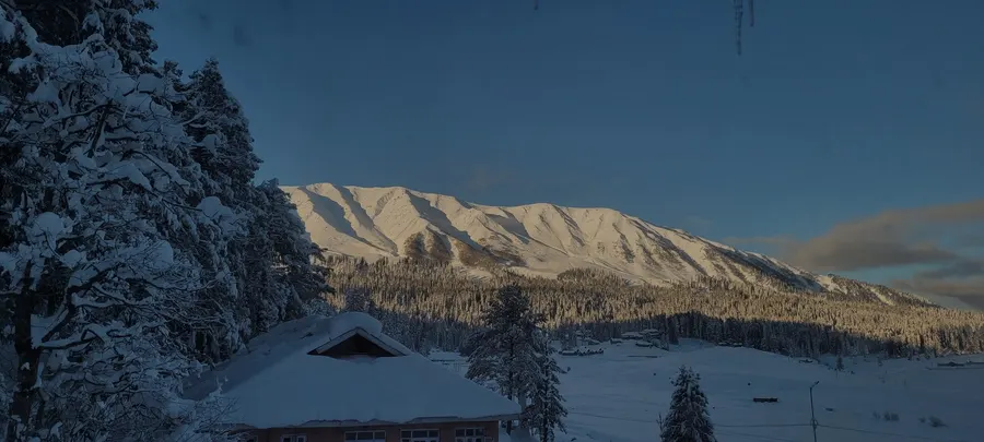 Snow-covered lodges beneath the Apharwat range at golden hour in Gulmarg